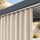 Outdoorvorhang in Hellelfenbein an weißer Vorhangschiene unter einer anthrazitfarbenen Pergola mit Lamellendach.